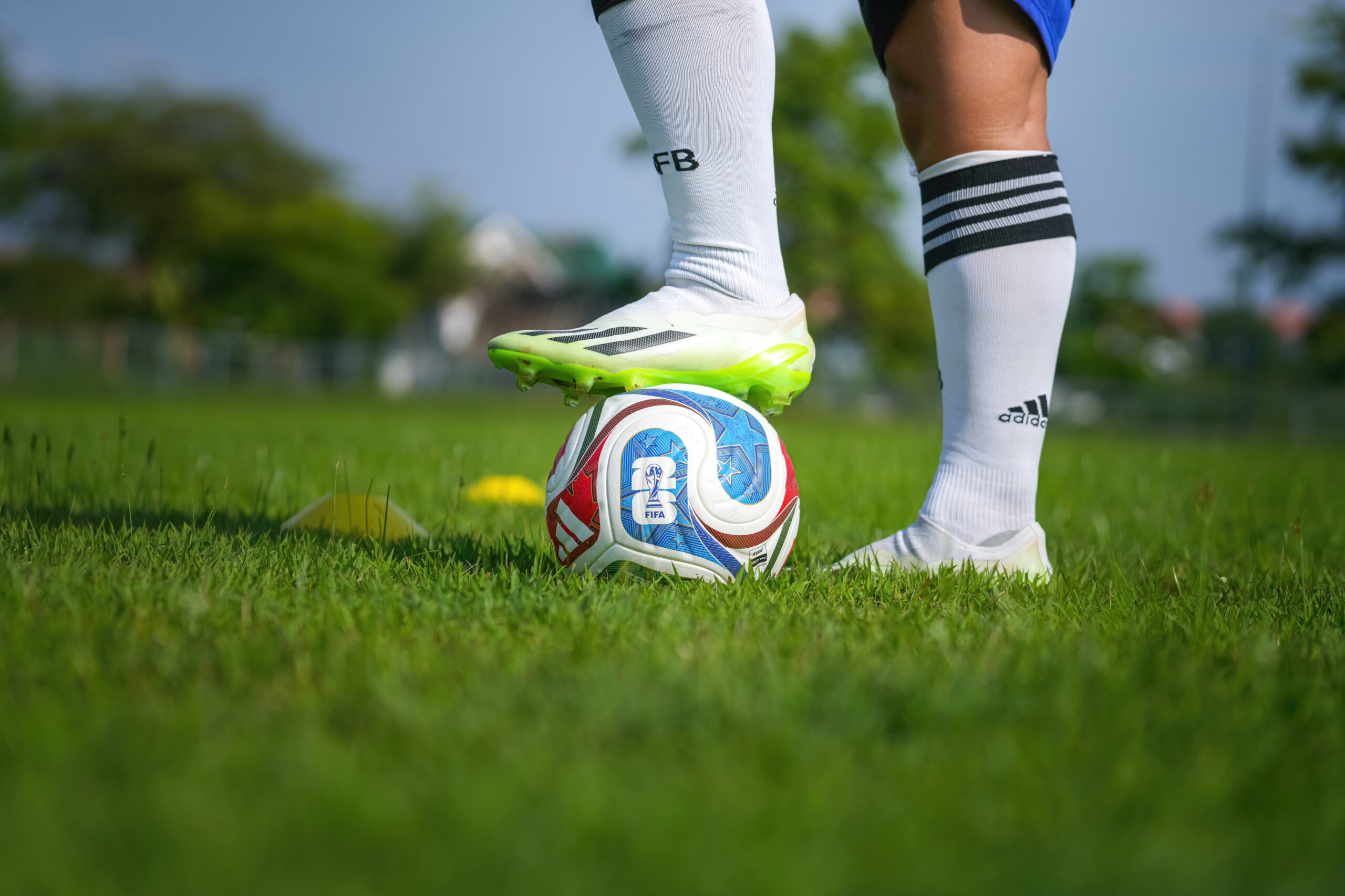 Soccer player balancing a colorful ball with their foot on a grassy field, wearing white socks and neon cleats.